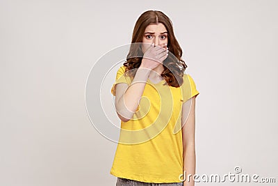 I won& x27;t say anyone. Frightened teenager girl in yellow T-shirt covering her mouth with arm, looking Stock Photo