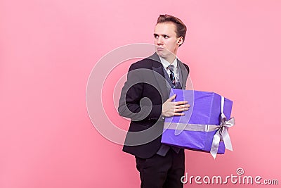I won`t share! Portrait of resentful greedy man in suit with stylish haircut holding big wrapped present. studio shot isolated, Stock Photo