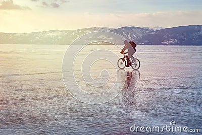 Ice biker traveler with backpacks on bike on ice of Lake Baikal. Against the background of sunset sky, ice surface. Winter sport Stock Photo