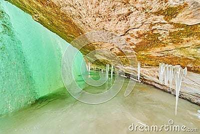 Ice cavern on frozen lake with entrance covered by frozen green waterfall Stock Photo