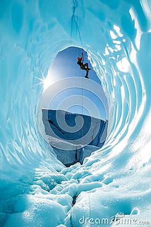 Ice climber ascending a rope over entrance of large blue ice cave on the Matanuska Glacier in Alaska Stock Photo