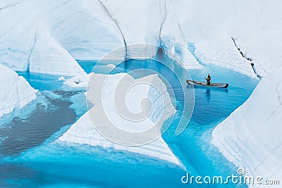 Ice climber canoeing narrow canyons and fins that look like icebergs in front of an ice cave in Alaska Stock Photo