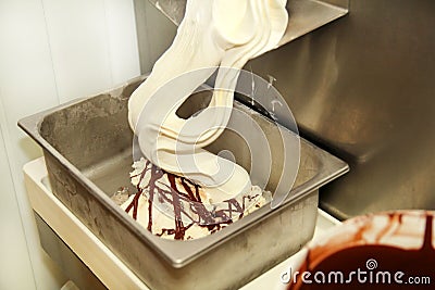 Ice cream making machine produces vanilla ice cream with chocolate dressing and it falls into steel container. Stock Photo