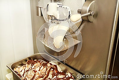 Ice cream making machine produces vanilla ice cream with chocolate dressing and it falls into steel container. Stock Photo