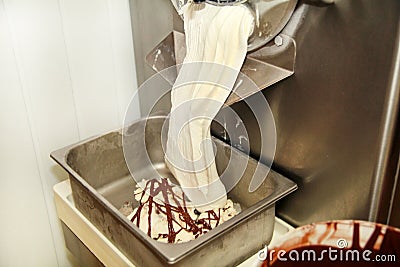 Ice cream making machine produces vanilla ice cream with chocolate dressing and it falls into steel container. Stock Photo