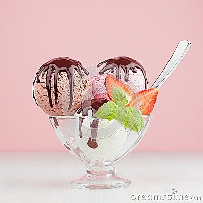 Ice cream scoops with slices strawberry, green mint, spoon, chocolate sauce in bowl in pink interior on white wood board. Stock Photo