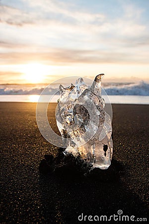 Ice crystal part piece iceberg glacial fragment on black sand ocean waves sunset Diamond Beach Jokulsarlon South Iceland Stock Photo