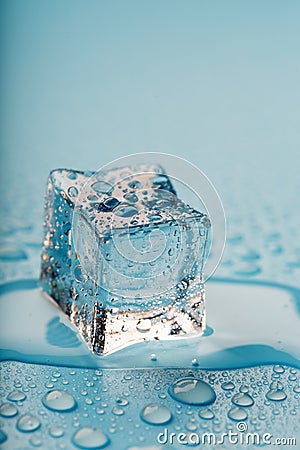 Ice cube with water drops on a blue background. The ice is melting Stock Photo