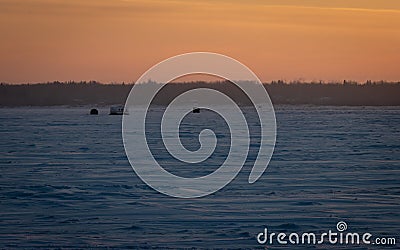 Ice fishing shacks on a frozen lake at sunset. Stock Photo