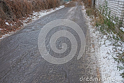 Ice on the gray asphalt road along the fence in the snow Stock Photo