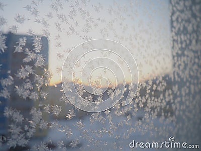 Ice patterns on the window. Beautiful curls and crystals on glass. Outside the window there is a blue winter sky, snow and a city Stock Photo