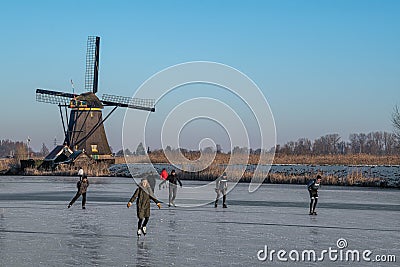 Ice skaters on a frozen windmill canal at sunrise moment Editorial Stock Photo