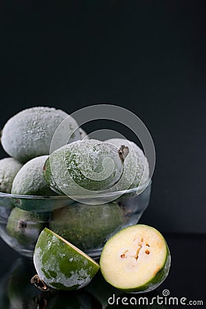 Iced frozen berries in bowl. Many whole green feijoa berries with cut one on black background Stock Photo