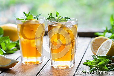 Iced tea with lemon slices and mint on wooden table with a view to the terrace and trees. Close up summer beverage Stock Photo