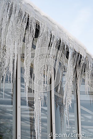 Icicles hang from roof and wall in winter. Frozen water from melting ice and snow during spring thaw Stock Photo