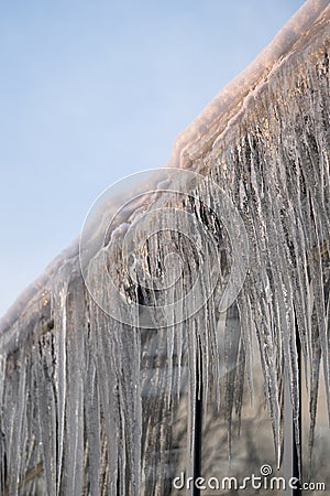 Icicles hang from roof and wall in winter. Frozen water from melting ice and snow during spring thaw Stock Photo