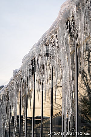 Icicles hang from roof and wall in winter. Frozen water from melting ice and snow during spring thaw Stock Photo