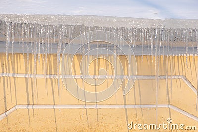 Icicles hanging from the roof of the house. Melting snow on the roof. Dangerous sharp transparent icicles hanging on the Stock Photo