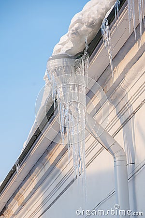 Icicles hanging from the roof of the house. Melting snow on the roof. Dangerous sharp transparent icicles hanging on the Stock Photo