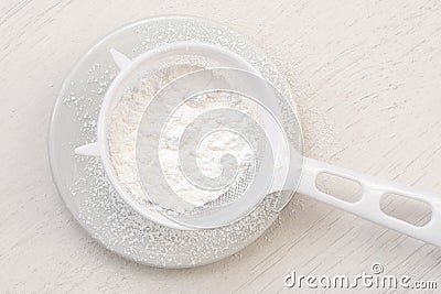 Icing sugar in a plastic sieve on top of white ceramic plate from above Stock Photo