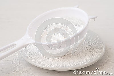 Icing sugar in a plastic sieve on top of white ceramic plate Stock Photo