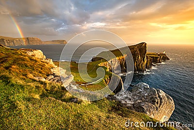 Iconic Isle of Skye lighthouse at Neist Point with beautiful golden light and rainbow over coast. Stock Photo