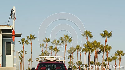 Iconic retro wooden lifeguard watch tower and baywatch red car. Life buoy, american state flag and palm trees against blue sky. Stock Photo