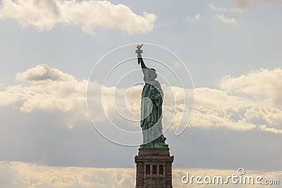 An iconic view of Statue of Liberty on Liberty Island in New York set against brilliant blue sky with fluffy white clouds Stock Photo