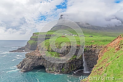 The iconic waterfall of Gasadalur on faroe islands and the remote village in the background Stock Photo