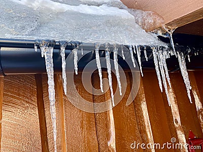 Icycles hanging from guttering on the side of a wooden house. Hovden, Norway, Feb 2023. Stock Photo