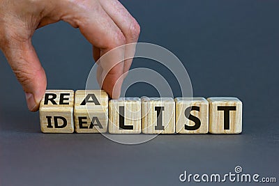 Idealist or realist. Male hand flips wooden cubes and changes the word `idealist` to `realist` or vice versa. Beautiful grey Stock Photo