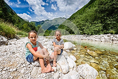 Identical twin girls sitting on river rock after nature hiking Stock Photo