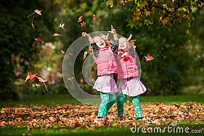 Identical twins having fun with autumn leaves in the park, blond cute curly girls, happy kids, beautiful girls in pink jackets Stock Photo