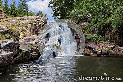 Idyllic mountain creek waterfall cascading down the cliff Stock Photo