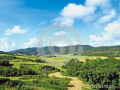 Idyllic panoramic view of tropical countryside with green hills with lush vegetation under tropical blue sky with white clouds. Stock Photo