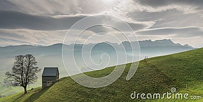 Idyllic and peaceful mountain landscape with a secluded wooden barn and lone tree on a grassy hillside and a great view of the Swi Stock Photo