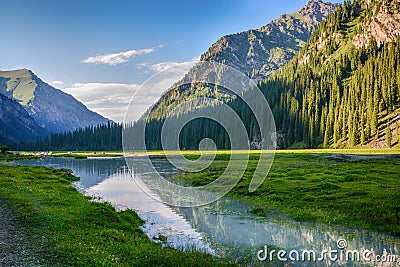 Idyllic summer landscape with hiking trail in the mountains with beautiful fresh green mountain pastures, river with reflection Stock Photo
