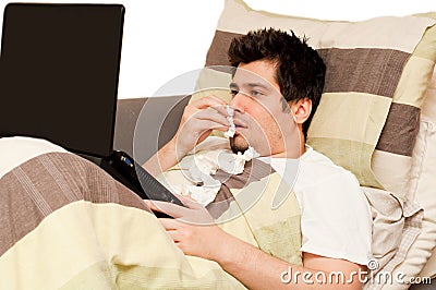 Ill guy with runny nose using laptop on the couch Stock Photo