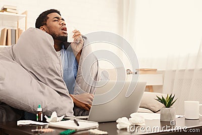 Ill man suffering from rhinitis working on couch with laptop Stock Photo