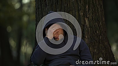 Ill man touching head, sitting under tree in park, sudden migraine attack insult Stock Photo