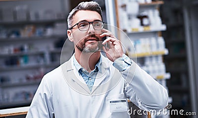 Ill prepare your medication for collection. a mature pharmacist talking on a cellphone in a pharmacy. Stock Photo