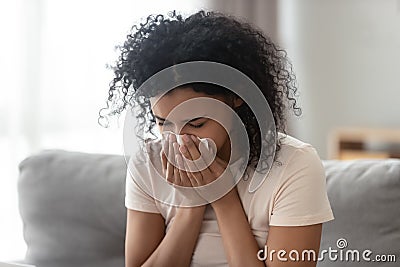 Ill allergic african woman blowing nose in tissue at home Stock Photo