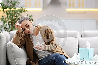 Ill woman with nasal spray and box of paper tissues on sofa at home Stock Photo