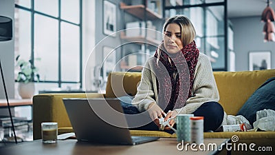 Ill Young Female Blowing Her Nose and Calling into Office with Video Phone Call from Cozy Living Stock Photo