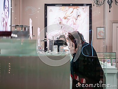 Illuminated billboard advertising in a jewelry and jewelry store. In the foreground, an elderly woman examines goods in a shop wi Editorial Stock Photo