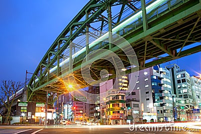 Illuminated buildings with advertising signs in a shopping district and train on elevated bridge Editorial Stock Photo