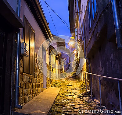 Illuminated cobbled street with light reflections on cobblestones in old historical city by night. Dark blurred Stock Photo
