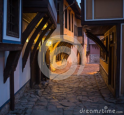 Illuminated cobbled street with light reflections on cobblestones in old historical city by night. Dark blurred Stock Photo