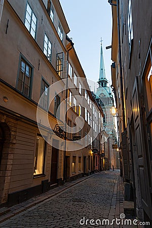 Illuminated cobbled street in the old town of Stockholm, Sweden at dusk with a church at the end Editorial Stock Photo