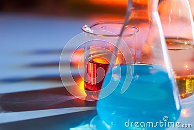 Illuminated laboratory flask filed with colorful chemical solutions with shadows on the table. Laboratory, science Stock Photo
